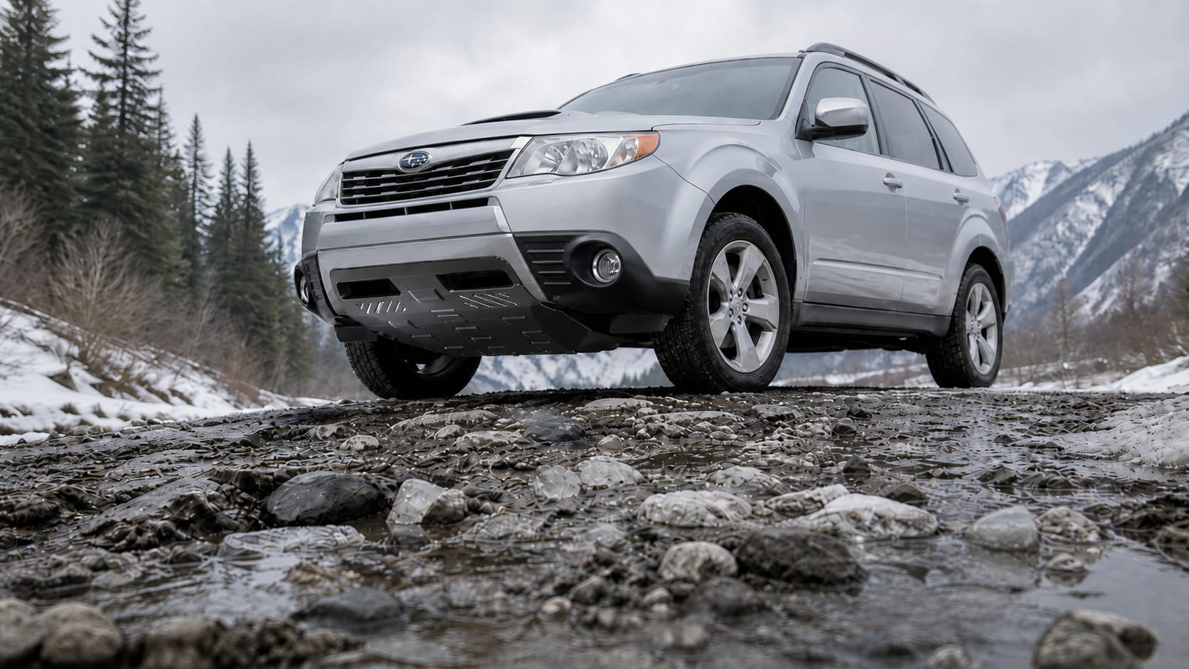 Subaru SUV with an underbody skid plate driving carefully on a snowy, damaged winter road with ruts, ice and road salt in the mountains